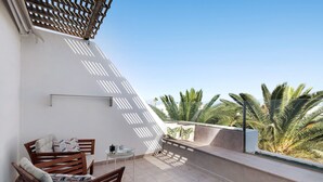 A balcony with a wooden chair, a small table, and a view of palm trees. - Vacation Apartment 'Los Molinos 4306' with Sea View, Private Pool and Wi-Fi (Costa Teguise)