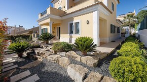 Una casa de estilo mediterráneo con tejado de baldosas, un balcón y un jardín con rocas y plantas.