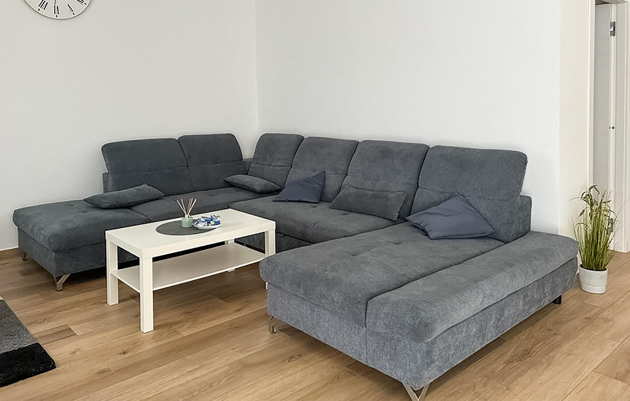 Un salon moderne avec un canapé d’angle gris, une table basse blanche et une petite plante.