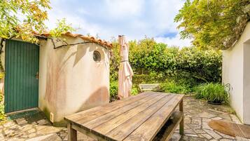 A wooden table in a stone-paved outdoor area with a green door and a small shed.