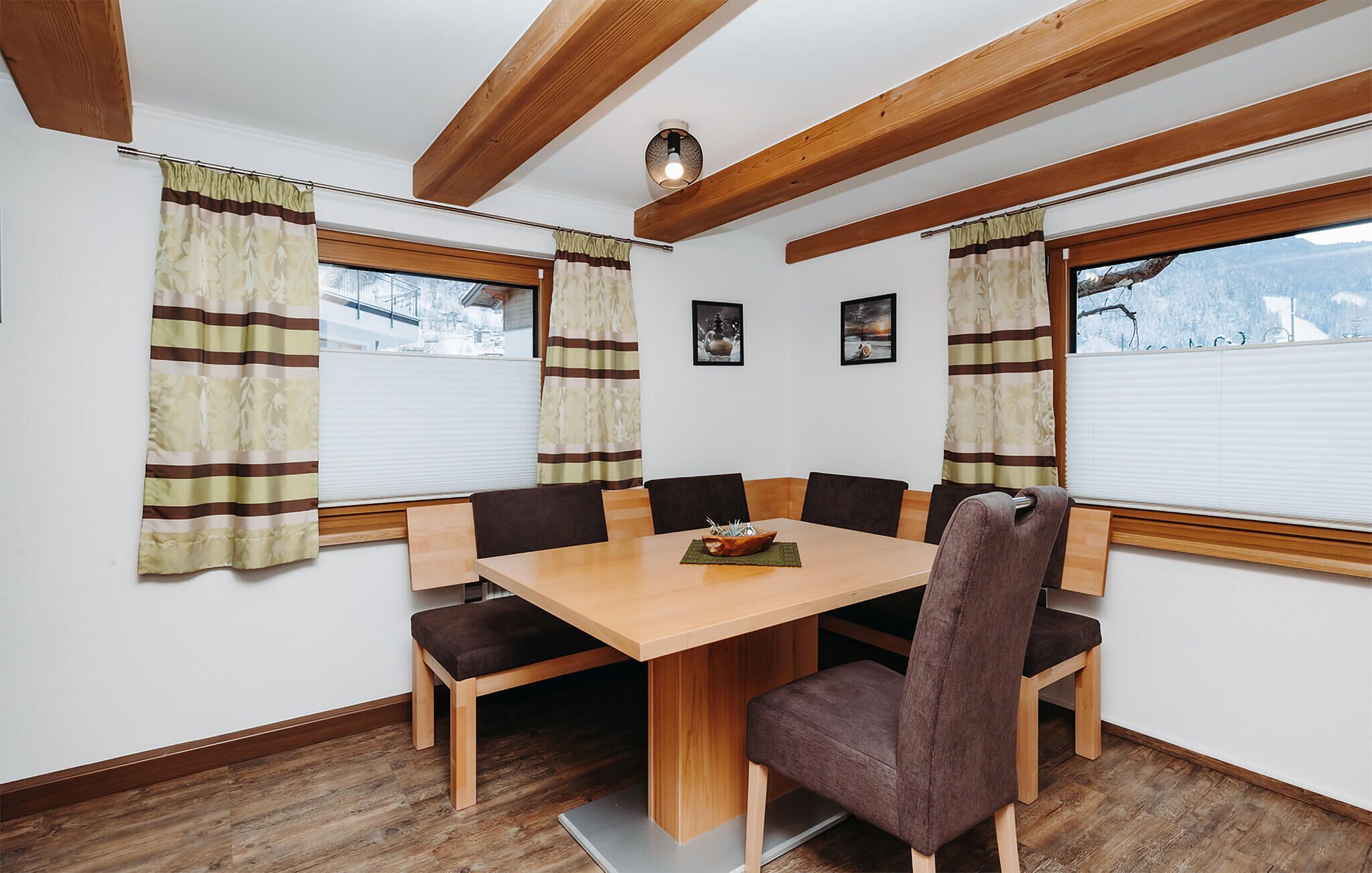 Un coin repas avec une table en bois et six chaises, une fenêtre avec des rideaux et un plafond avec des poutres apparentes.