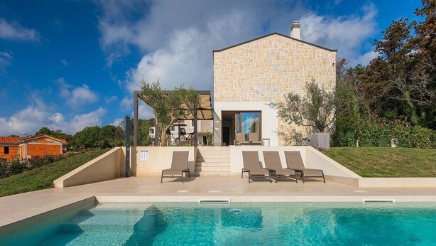 Ein modernes Haus mit Steinaußenwand, einem Swimmingpool und einer Terrasse mit Liegestühlen.