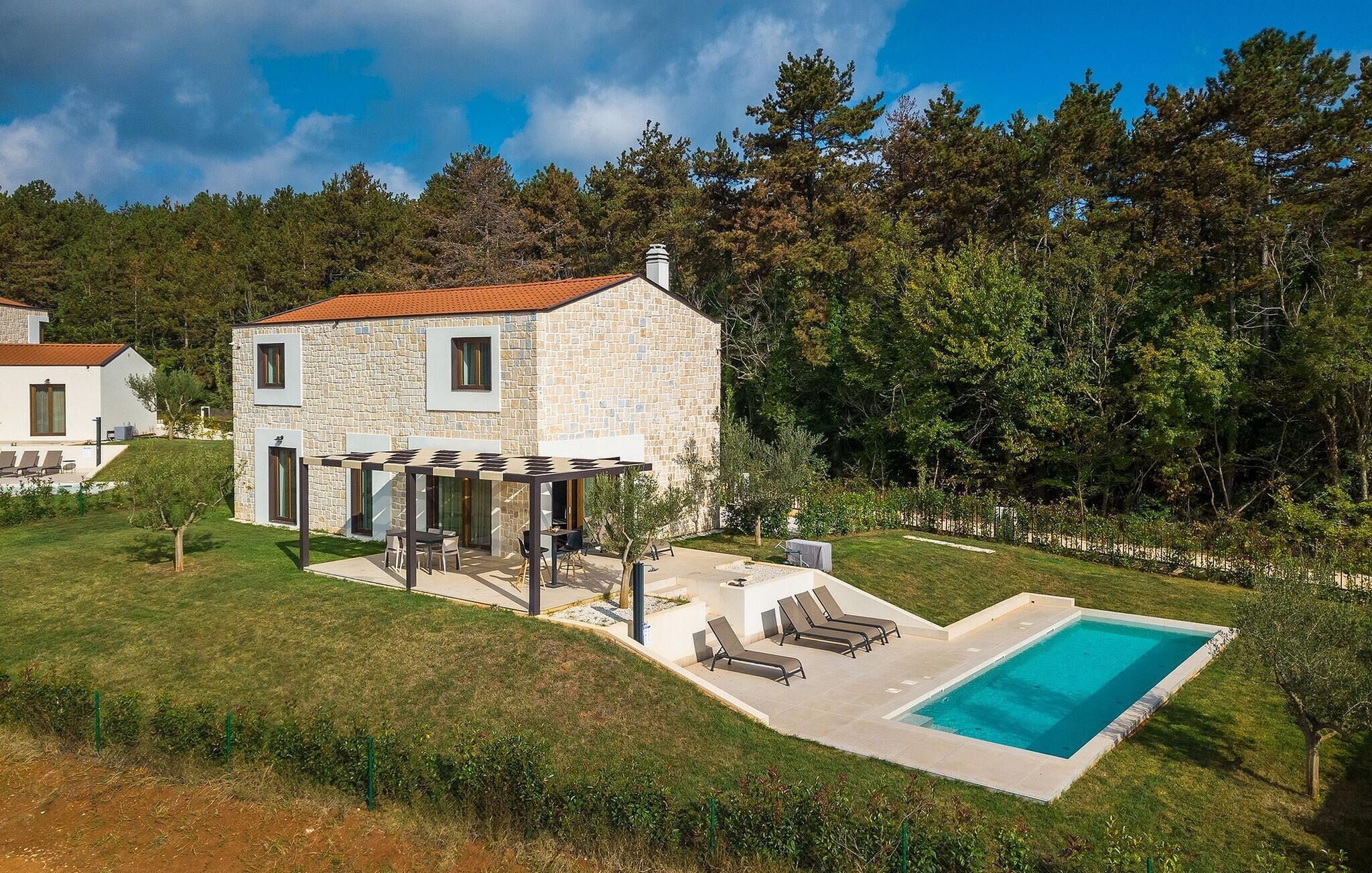 Una casa de piedra con piscina, mobiliario exterior y una pérgola.