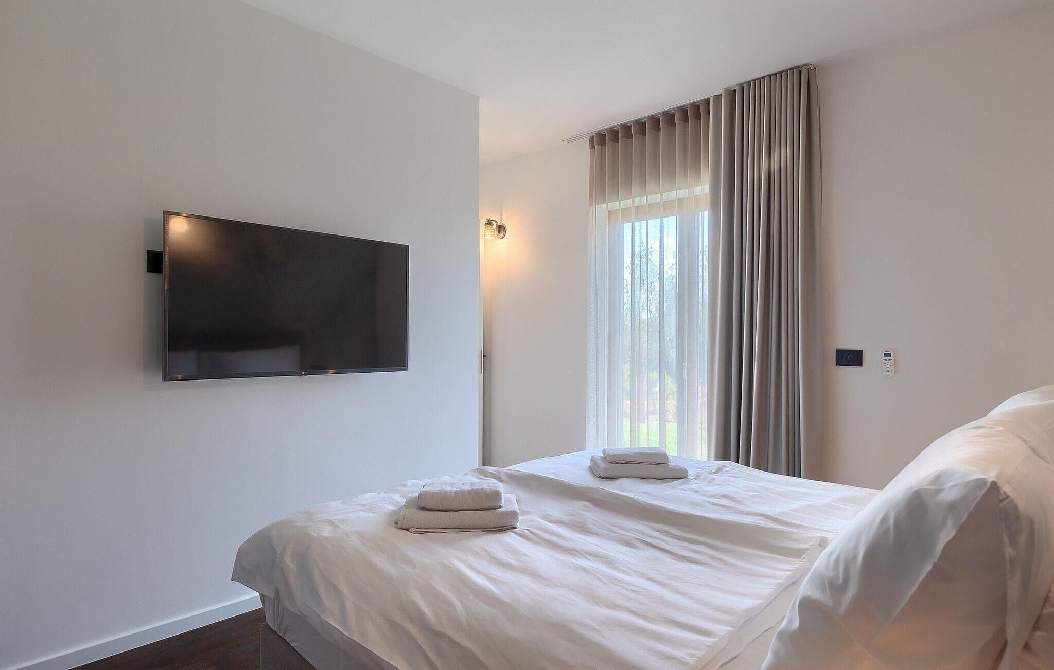 Ein Hotelzimmer mit Bett, Wandfernseher und einem Vorhangfenster.