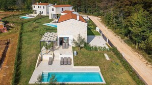 Ein modernes, zweistöckiges Haus mit Swimmingpool, Natursteinfassade und gepflegtem Rasen.