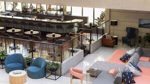 Un área lounge moderna con un bar, diferentes disposiciones de asientos y una escalera que sube a un nivel superior.