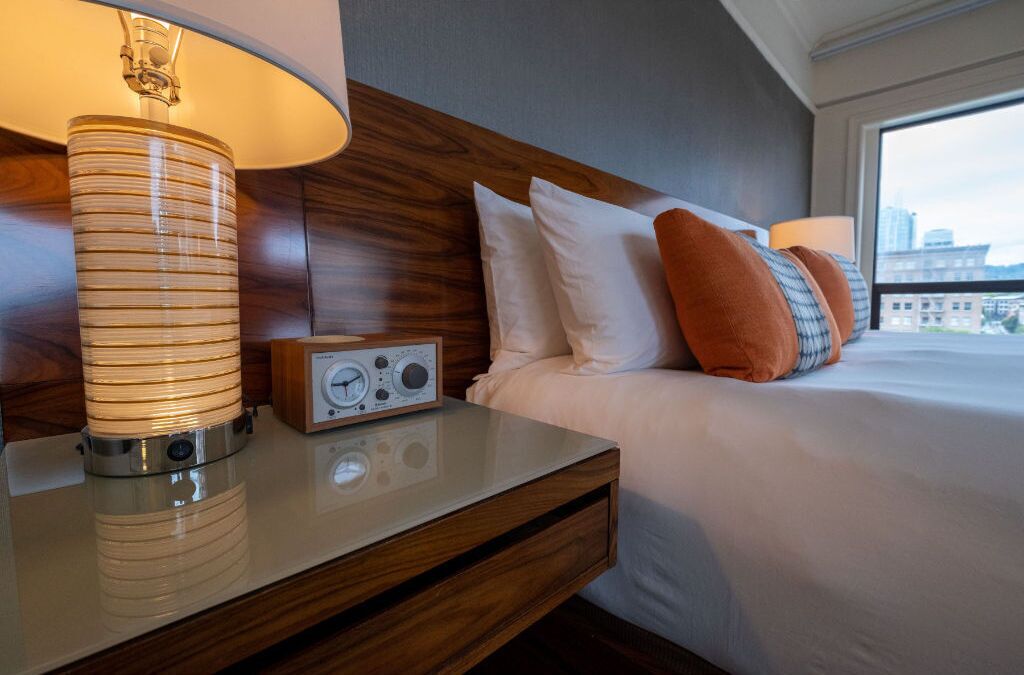 Una habitación de hotel con una cama, una mesita de noche con lámpara y un radio.