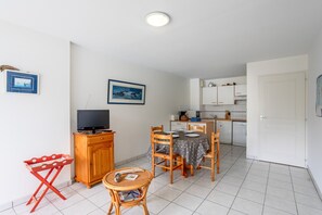 Un espacio habitable compacto con comedor, televisor, pequeña cocina y una puerta que da a otra habitación.