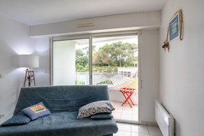 Un salon comprenant un canapĂ©, une lampe, un radiateur et une porte-fenĂȘtre coulissante donnant sur un espace extĂ©rieur avec un fauteuil de patio.