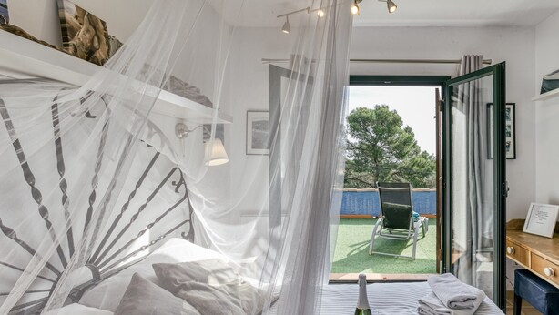 Ein Schlafzimmer mit einem Bett, einem Nachttisch, einem Stuhl, einer Glastür, die nach draußen führt, und Blick ins Freie.