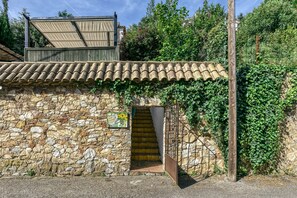 A stone building with a tiled roof, a staircase, and a wooden gate.