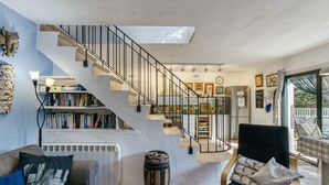 Eine Treppe führt zu einer zweiten Etage, ein Bücherregal, ein Heizkörper, ein Stuhl und ein Fenster mit Blick.