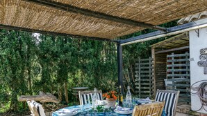 Ein Essbereich im Freien mit einem Tisch für vier Personen, umgeben von Stühlen, unter einer beschatteten Pergola.