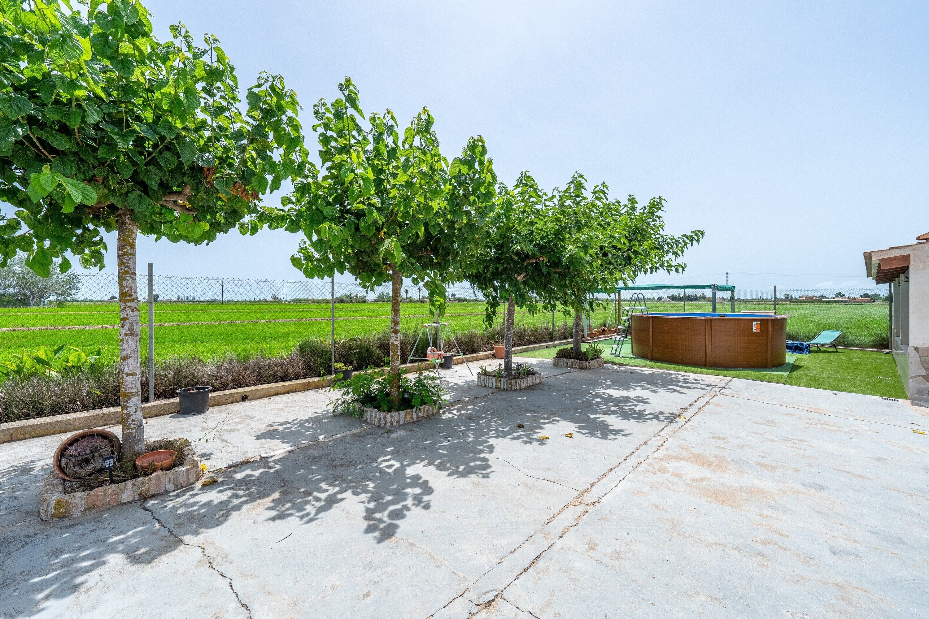 A patio with planters, a hot tub, and a view of a green field.