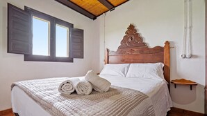 A neatly made bed with a quilted blanket and rolled towels, a wooden headboard, a small wooden shelf, and a window with shutters. - Country House 'Benjamin' with Lake View, Private Pool and Wi-Fi (Deltebre)