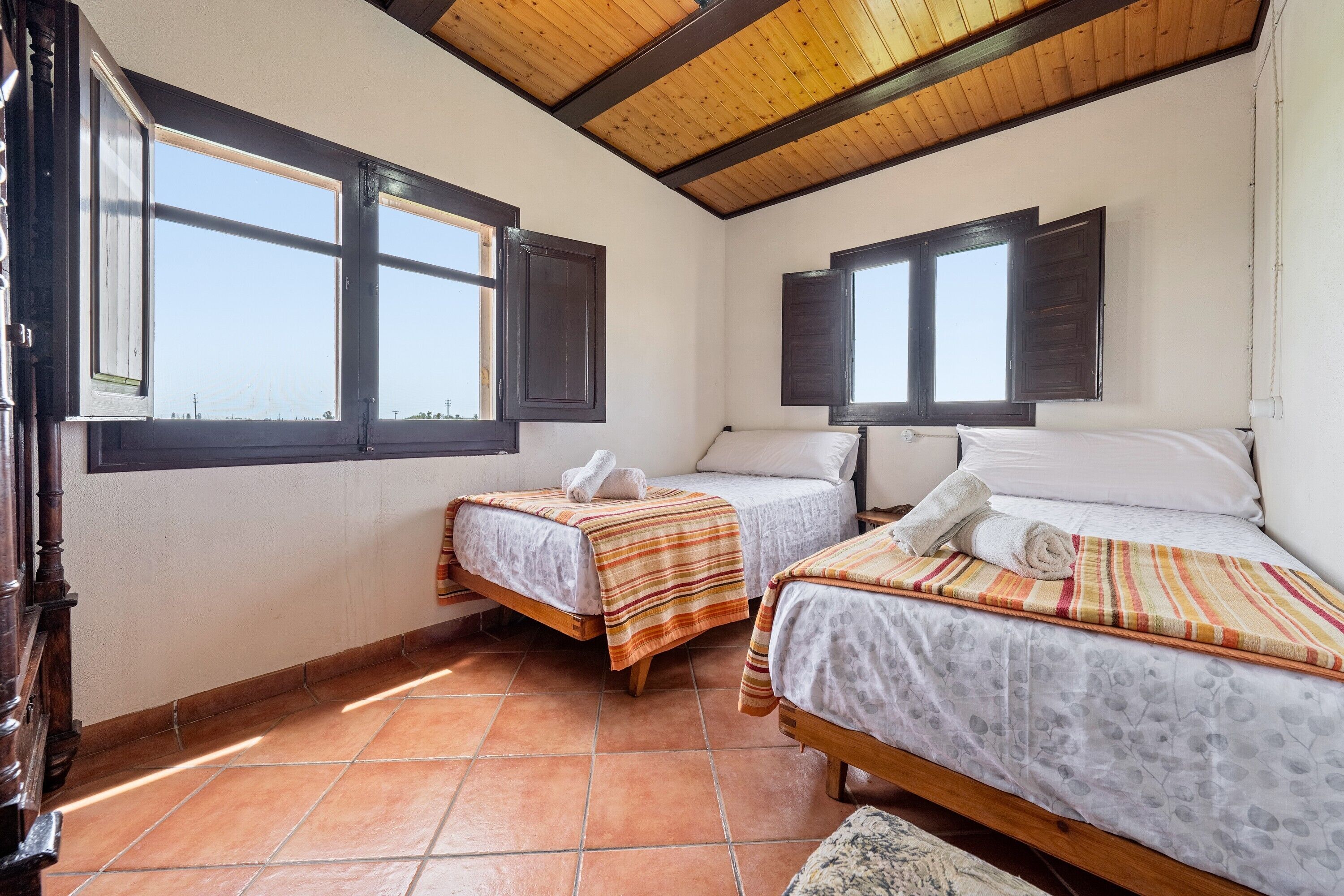 A room with two beds, wooden beams on the ceiling, and large windows.