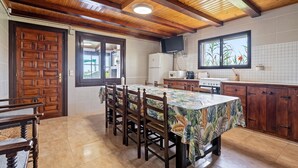 A kitchen with wooden ceiling beams, a dining table with chairs, a refrigerator, and a window with a view of plants. - Country House 'Benjamin' with Lake View, Private Pool and Wi-Fi (Deltebre)