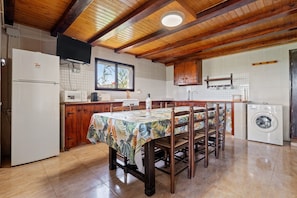 Una cocina con vigas de madera, una mesa de comedor con sillas, un refrigerador, una lavadora y una ventana con vistas.