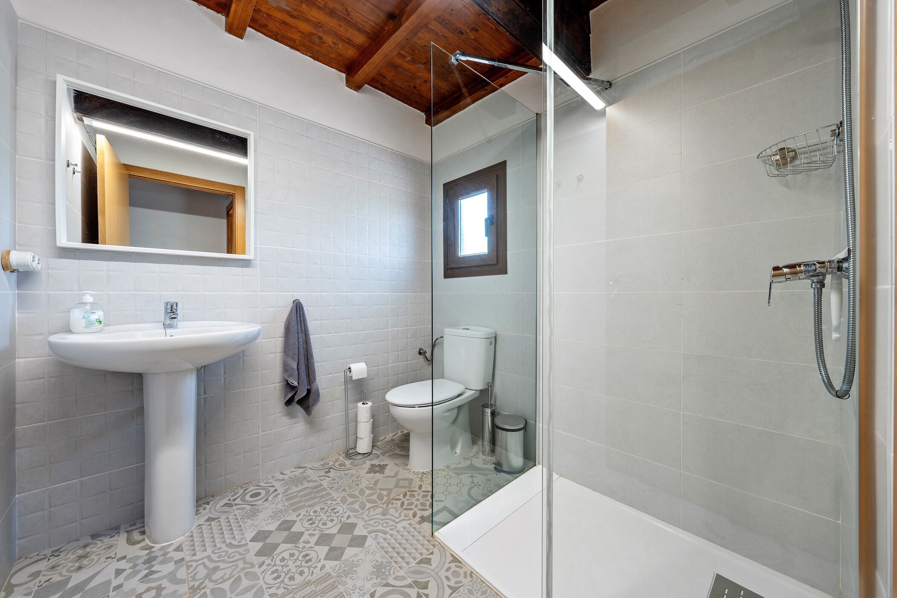 Un baño con lavamanos pedestal, inodoro, ducha y baldosas de suelo estampadas.
