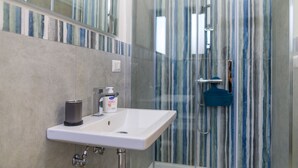 Ein Badezimmer mit weißem Waschbecken, einem Spiegel und einer Dusche mit gestreiftem Glas.