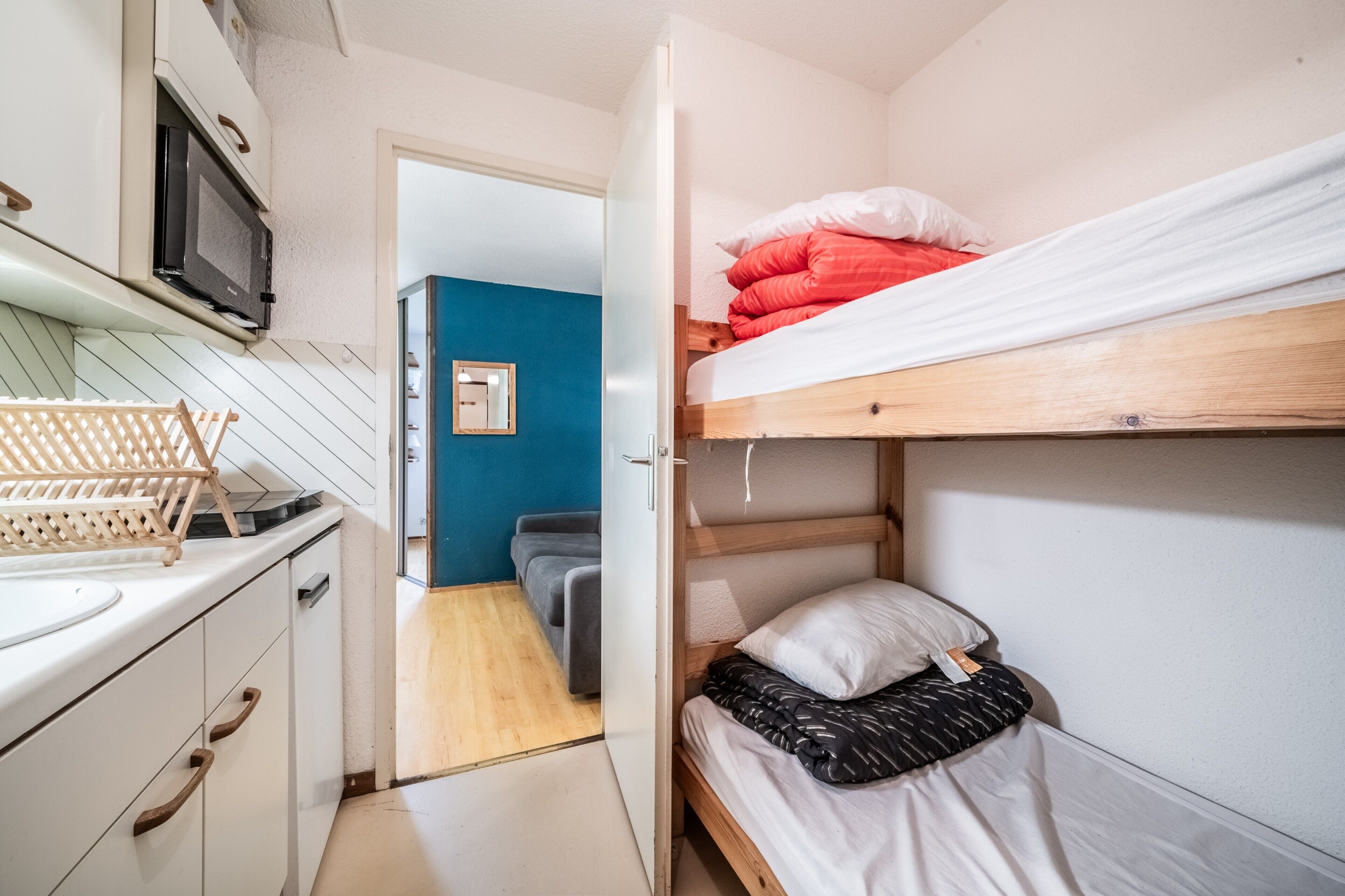 Een kleine kamer met een stapelbed, een kitchenette met een magnetron en een houten vloer.