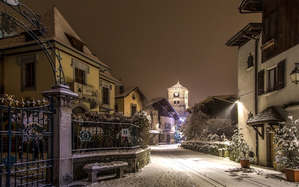A snow-covered street with buildings, a gate, and a tower in the distance.