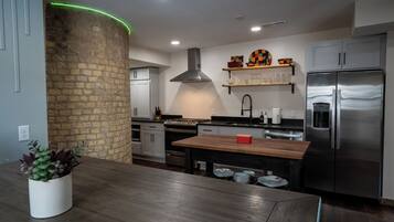A modern kitchen with a central island, stainless steel appliances, and a brick accent wall.