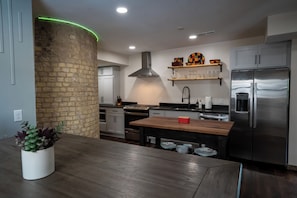 Een moderne keuken met een centraal eiland, roestvrijstalen apparatuur en een accentmuur van baksteen.