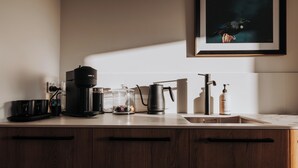 A kitchen with a coffee maker, a kettle, a sink, and a framed picture on the wall. - Ahuru House a touch of luxury - Tui Room (Mangawhai)