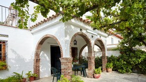 A courtyard with a white building featuring brick arches, potted plants, and a table with chairs. - Holiday Home 'Casa Rural La Encina' with Mountain View, Private Pool and Air Conditioning (Jaén)