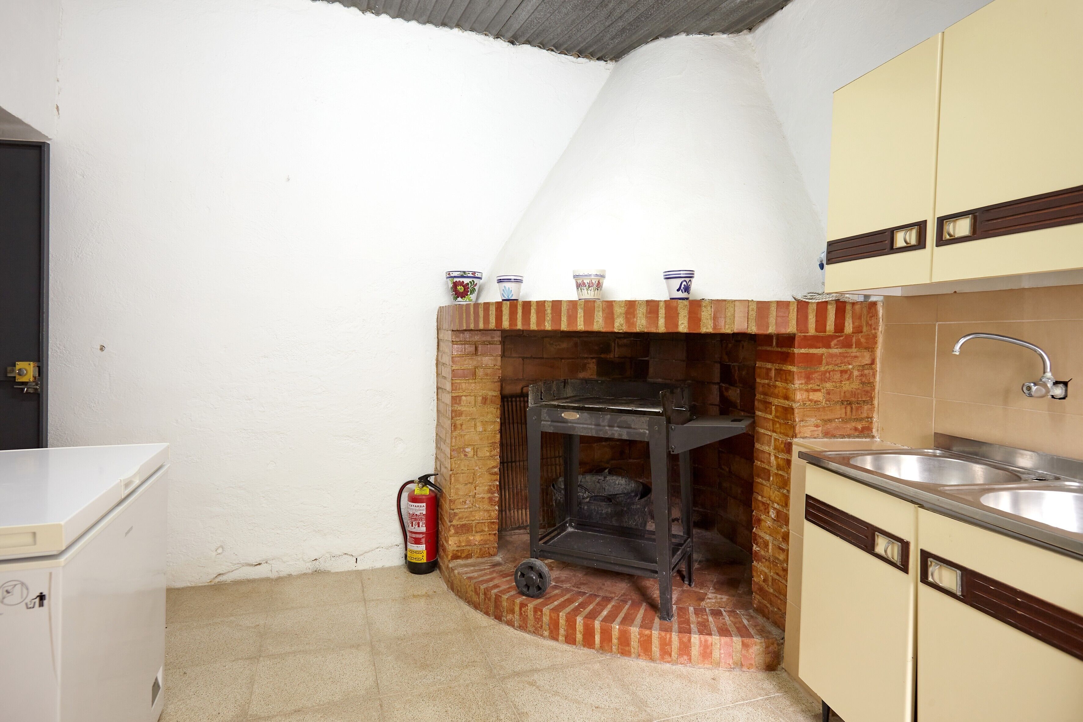 A compact kitchen with a brick fireplace, a sink, and a fire extinguisher.