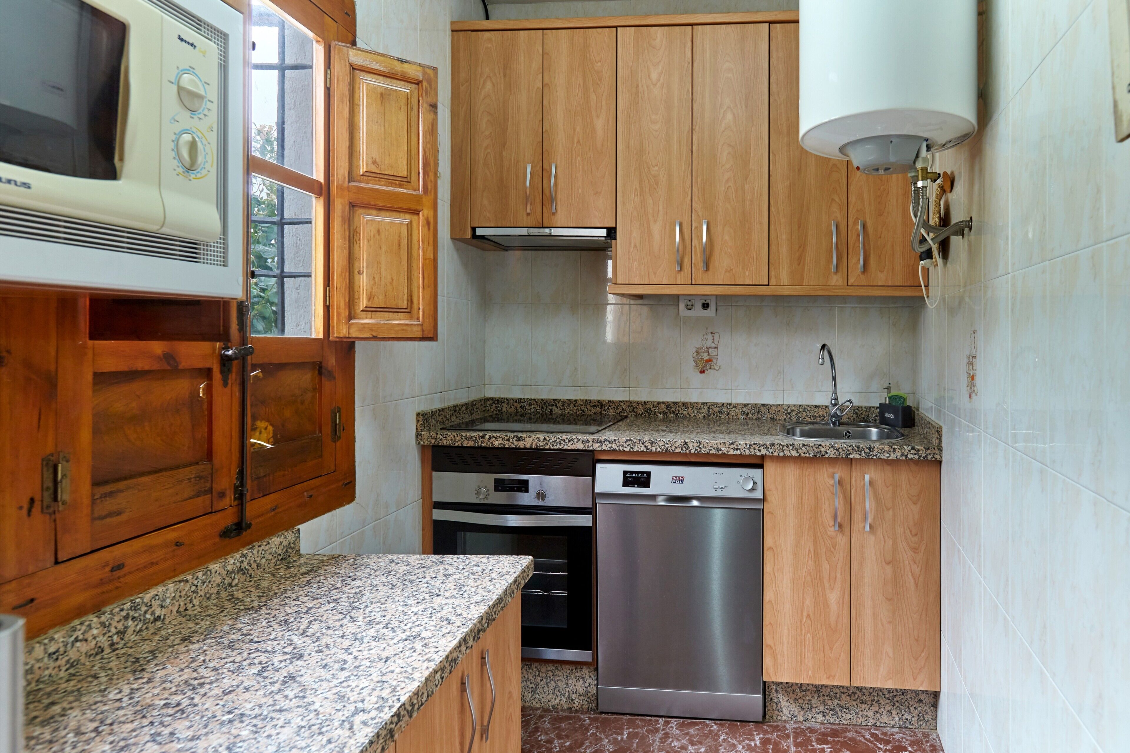 A kitchen with wooden cabinets, a built-in microwave, an oven, a dishwasher, granite countertops, and a stainless steel sink.