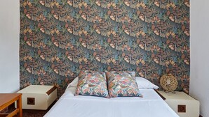 A bed with two patterned pillows, a bedside table, and a wall with a floral wallpaper pattern. - Holiday Home 'Casa Rural La Encina' with Mountain View, Private Pool and Air Conditioning (Jaén)