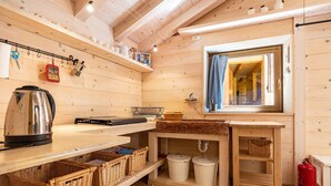 A wooden cabin interior with a kitchen area, a window with a view, and a red fire extinguisher. - Wunderchalet with Mountain Views, Private Grounds, and Terrace (valdaone)