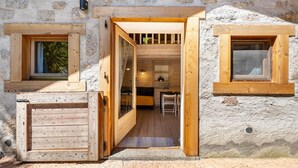 A rustic stone building with wooden doors and windows, a small kitchen area, and a seating space. - Wunderchalet with Mountain Views, Private Grounds, and Terrace (valdaone)