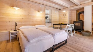 A wooden cabin-style room with two beds, a table, chairs, a stove, and a small shelf with a plant. - Wunderchalet with Mountain Views, Private Grounds, and Terrace (valdaone)
