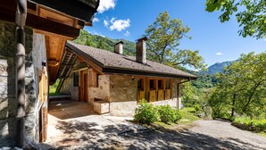 A rustic stone building with a wooden porch, a chimney, and a view of a mountainous landscape. - Wunderchalet with Mountain Views, Private Grounds, and Terrace (valdaone)