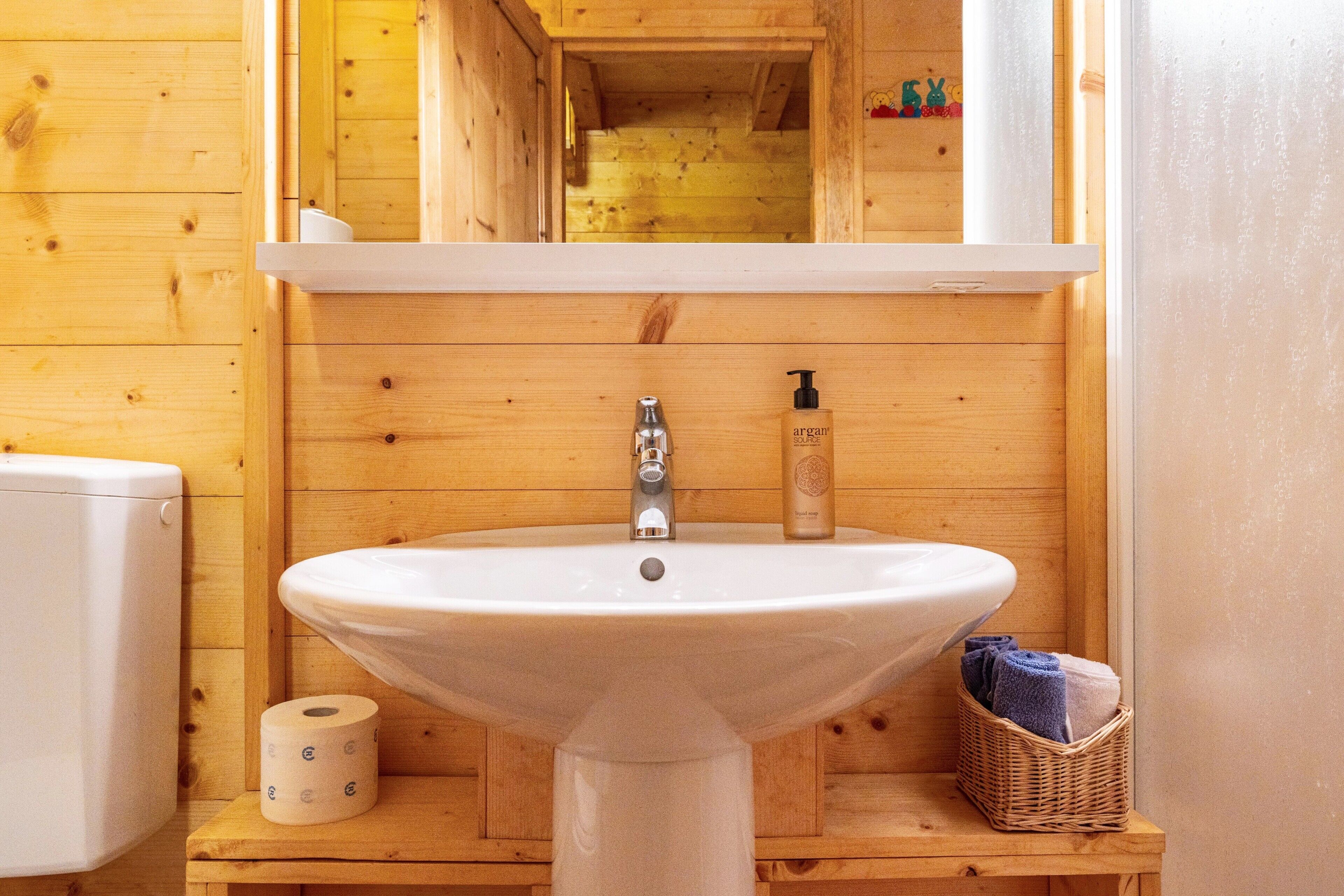 A wooden cabin bathroom with a white sink, toilet, and a mirror above the sink.