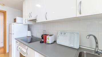 Una cocina con armarios blancos, un lavamanos de acero inoxidable, un tostador y una tetera.