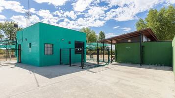Un edificio verde con área cercada, una ventana pequeña y una puerta.