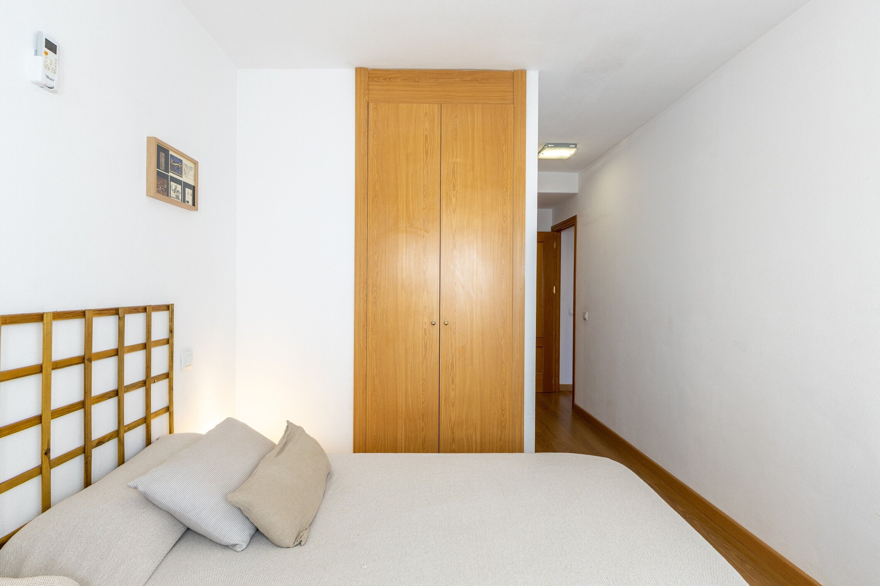 Un dormitorio con cabecera de madera, una cama con dos almohadas, un armario de madera y un pequeño cuadro en la pared.