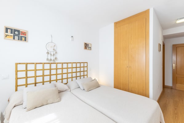A bedroom with a wooden headboard, a bed with white bedding, a wooden wardrobe, and a dreamcatcher on the wall.