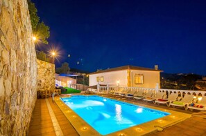 Una piscina amb gandules, una paret de pedra i un edifici amb llums.