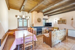 Un coin repas avec une nappe à carreaux, des chaises en bois, un canapé, une cheminée et un téléviseur.