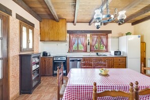 Une cuisine avec des meubles de rangement en bois, une cuisinière, un four à micro-ondes et une table recouverte d’une nappe à carreaux.