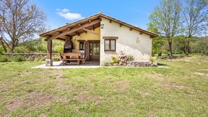 A rustic house with a wooden porch, a stone wall, and a clear blue sky.
