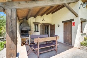 Une terrasse extérieure avec une table et des bancs en bois, un barbecue et un mur en pierre.
