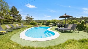 A swimming pool with lounge chairs and a table, surrounded by green grass and trees.