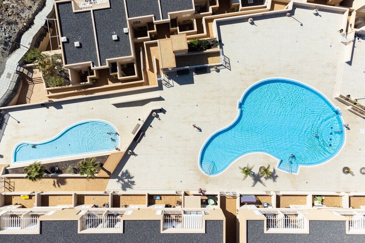A rooftop swimming pool area with two pools, a sun terrace, and a view of the surrounding buildings.