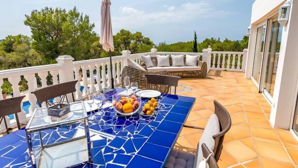 A terrace with a table set for dining, outdoor seating, and a view of the surrounding greenery.